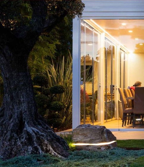 Diffusore a forma di roccia illuminato accanto a un ulivo, all'ingresso di una veranda