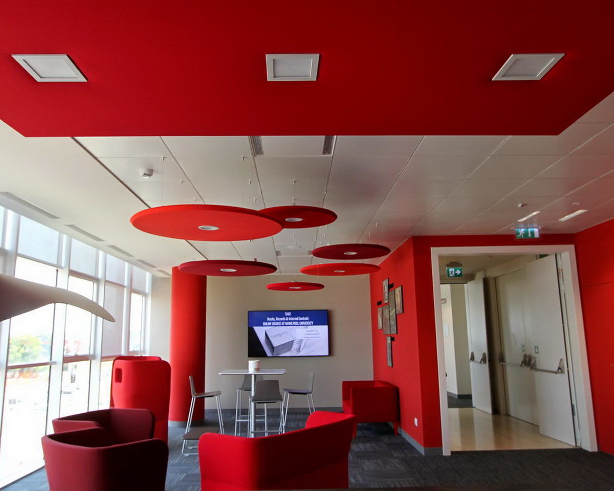Dischi acustici rossi sospesi a soffitto con illuminazione integrata in un'area lounge aziendale